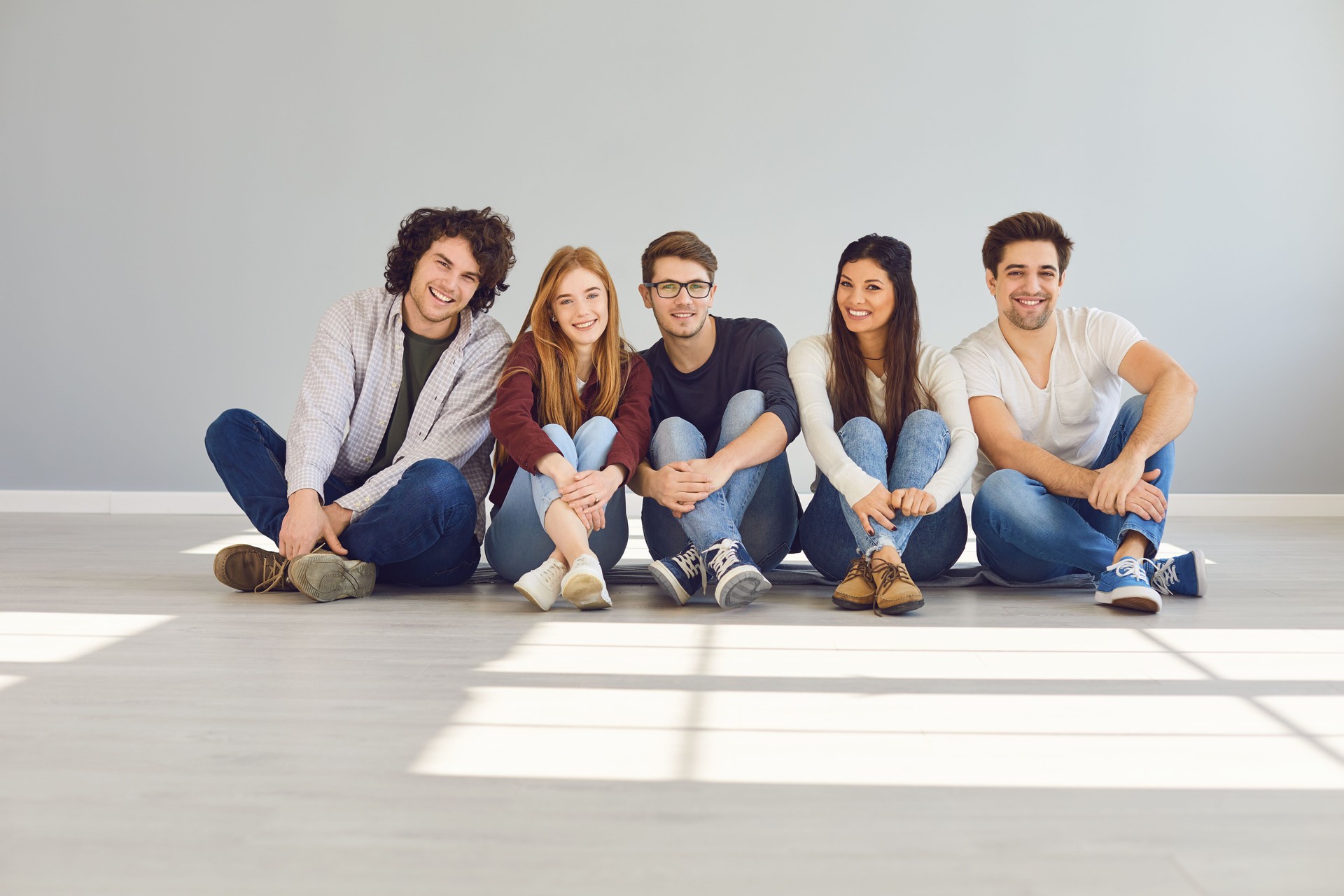 A group of friends is sitting on the floor in a room on a gray background.